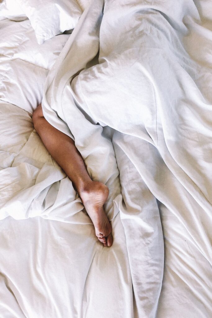 Frau liegt mit ausgestreckten Beinen im Bett