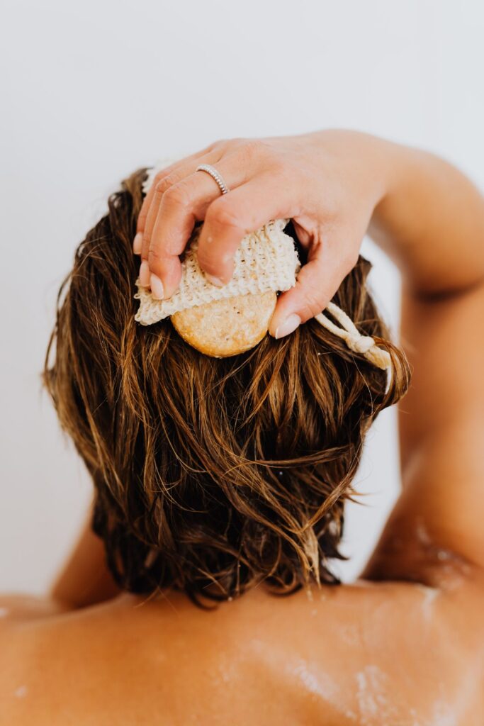 Eine Frau mit kurzen Haaren fährt mit einem Kopfhautschwamm über nasse Haare.