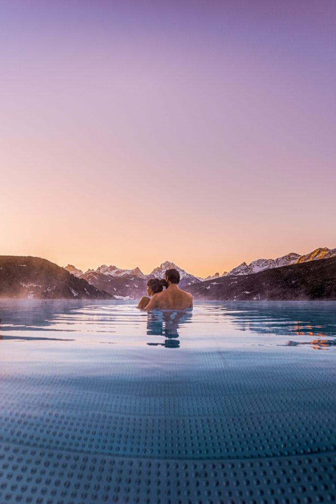 Hotel Alpen Tesitin ein Paar schwimmt im Pool bei Sonnenuntergang