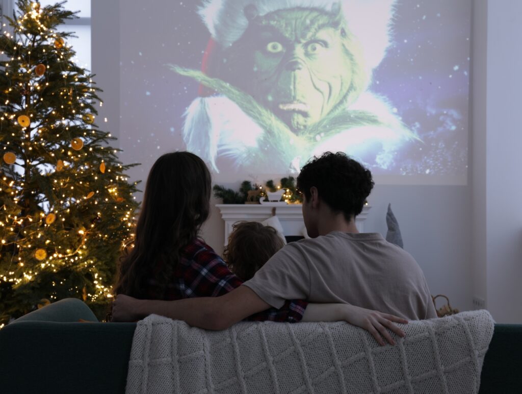 Eine Familie sieht über einen Beamer einen Weihnachtsfilm. Daneben steht ein 