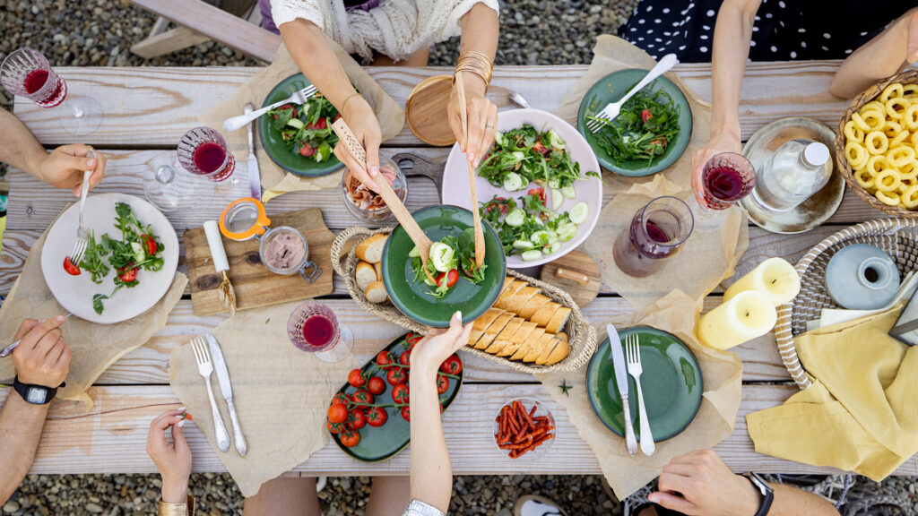 Sommerrezept: Bild von oben von einem Tisch mit Salaten, Brot, Tomaten und essenden Menschen