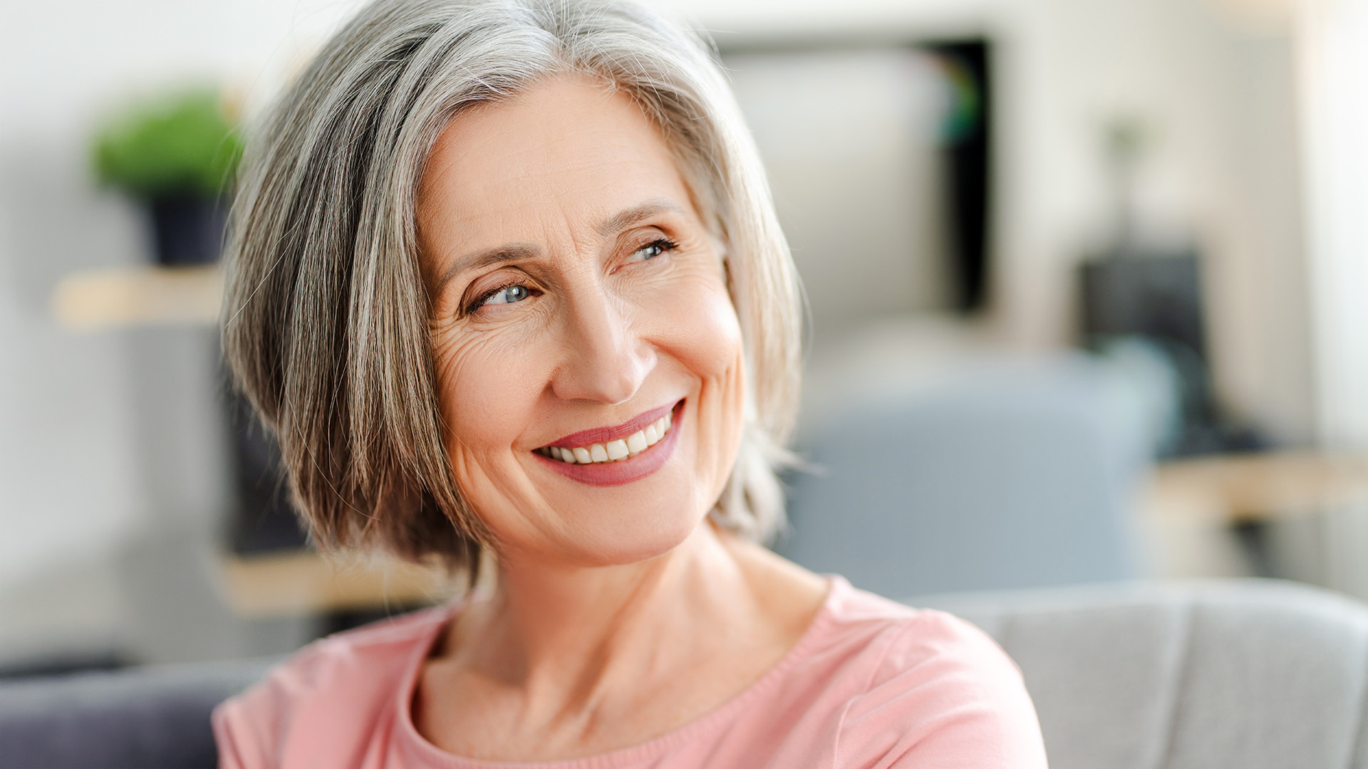 Wechseljahre: Lachende ältere Frau mit grauen Haaren vor pinkem Hintergrund