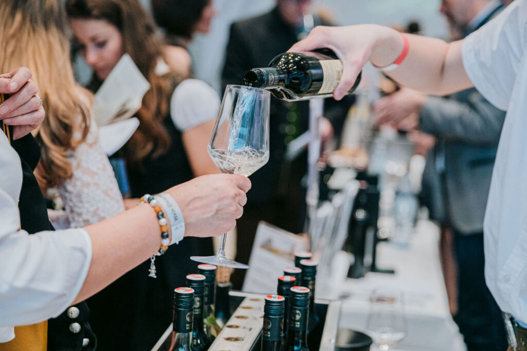 Verkostung von Riedenwein: Ein Mann schenkt in ein Weinglas ein mit vielen Leuten im Hintergrund.