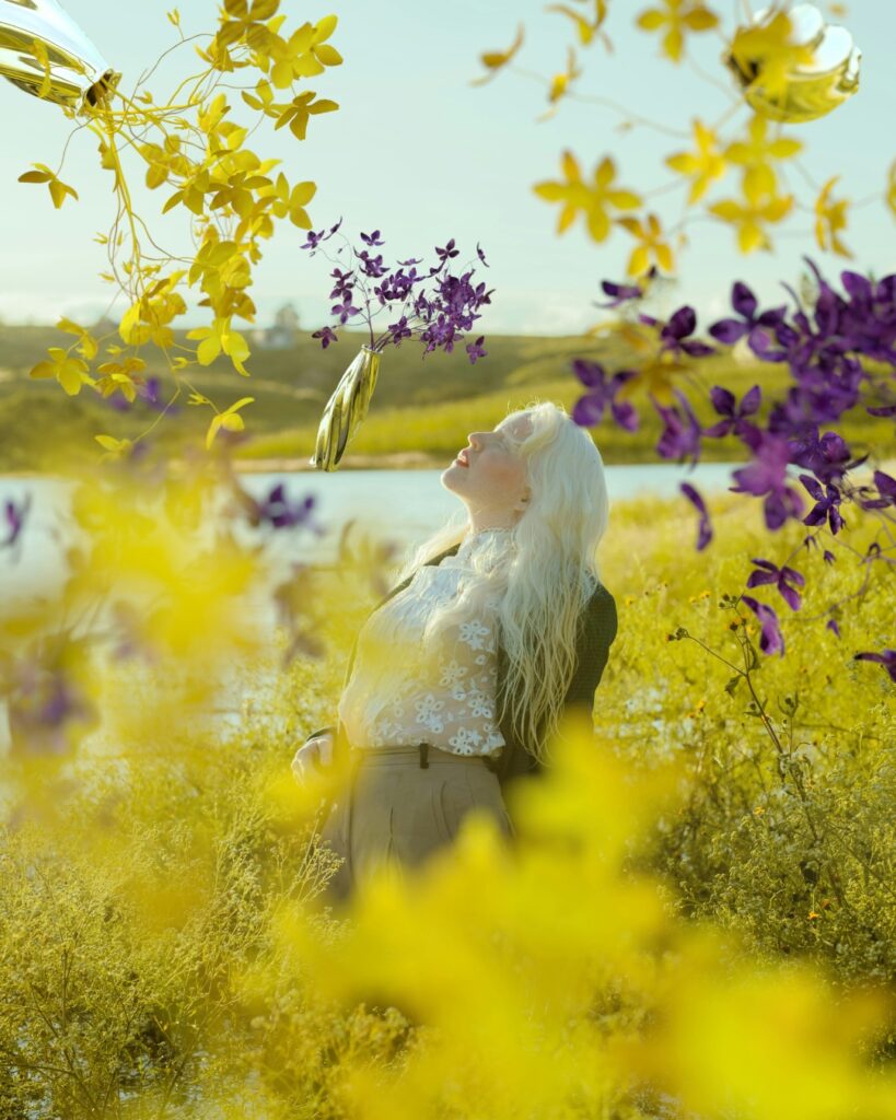 ästhetisches Naturfoto mit blonder Dame, die umgeben ist von lila Blumen