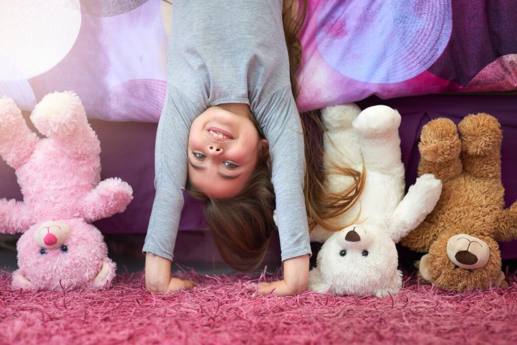Langeweile Kinder: Lachendes Mädchen steht mit Kuschelbären Kopf.