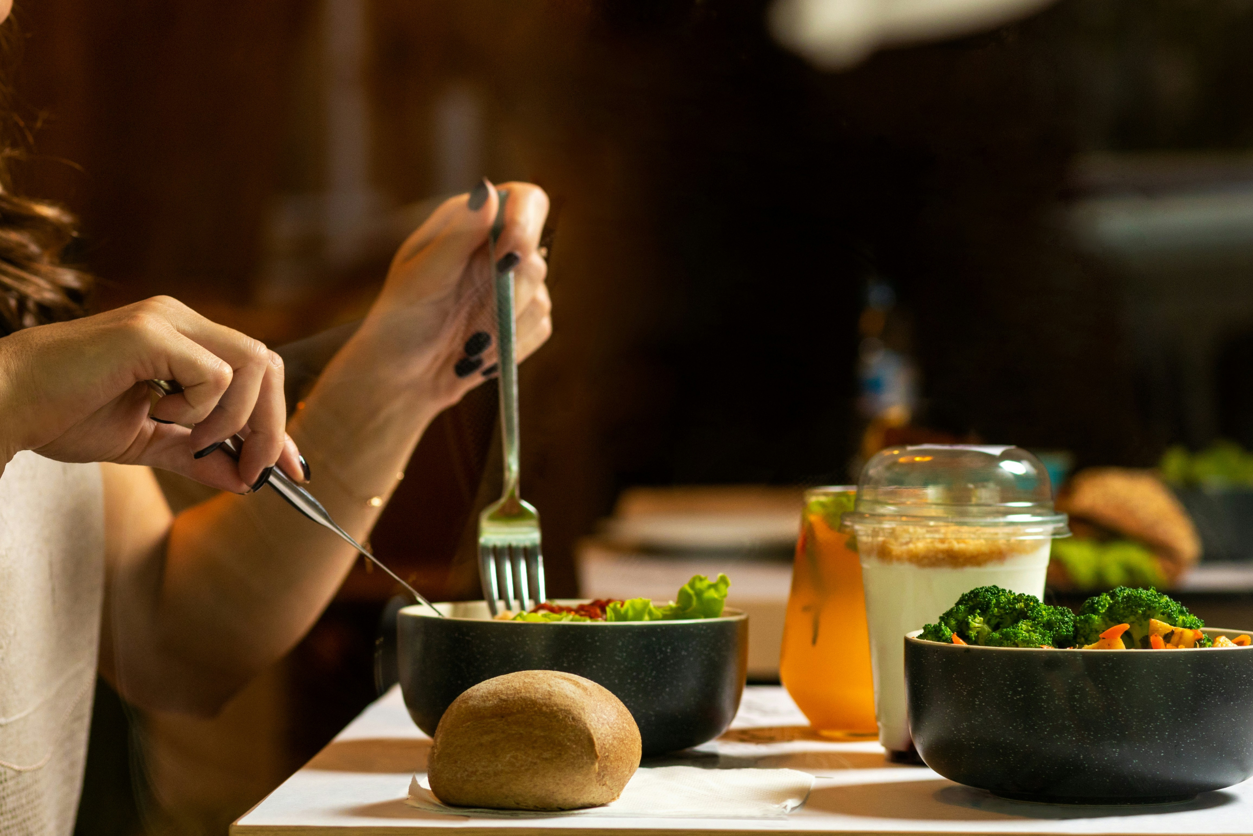 Herzgesundheit und Ernährung, Symbolfoto Tisch mit Essen, Besteck, Frau schneidet Essen auf